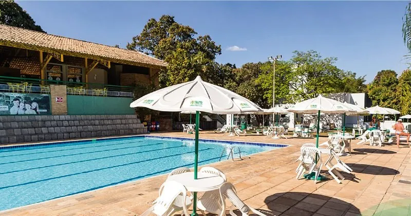 Área da piscina com ombrelones e o restaurante ao fundo